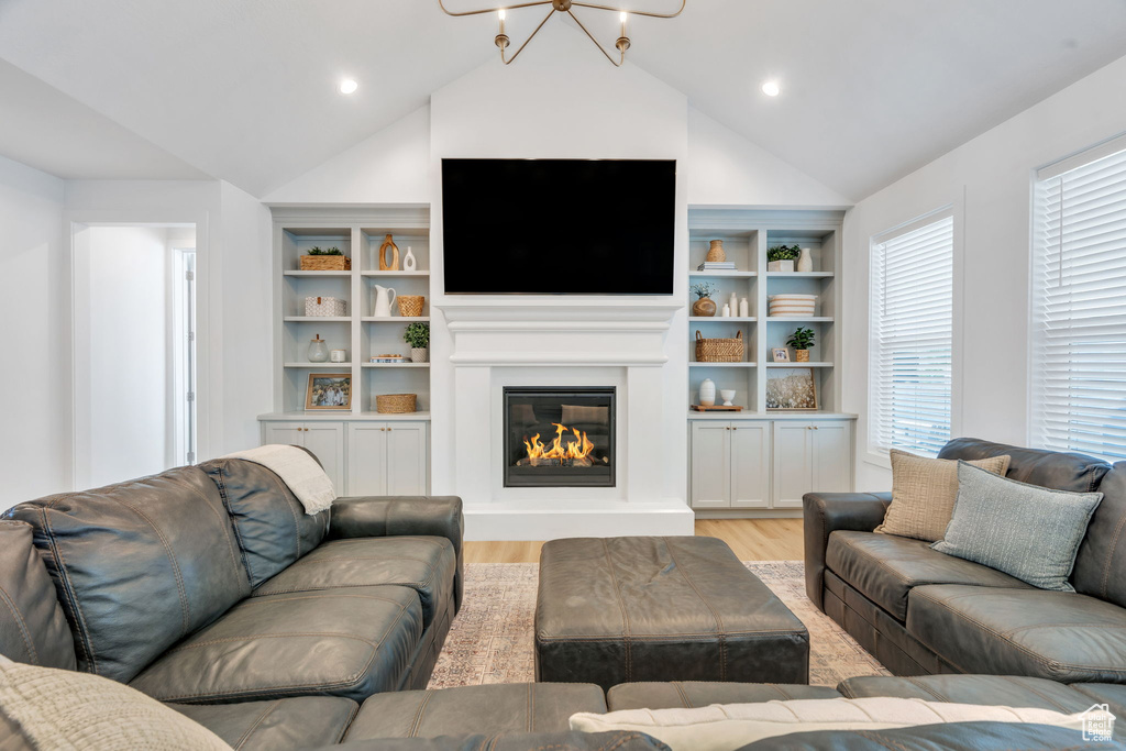 Living area with light wood-type flooring, vaulted ceiling, a glass covered fireplace, built in shelves, and recessed lighting
