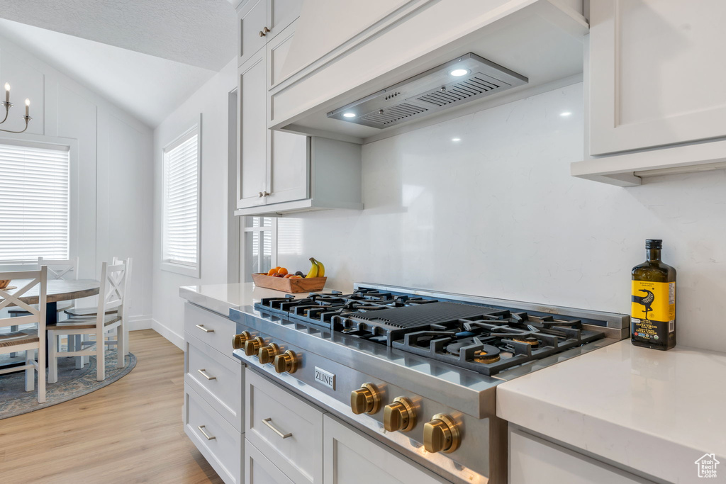 Kitchen featuring stainless steel gas stovetop, light wood-style floors, light countertops, white cabinets, and vaulted ceiling