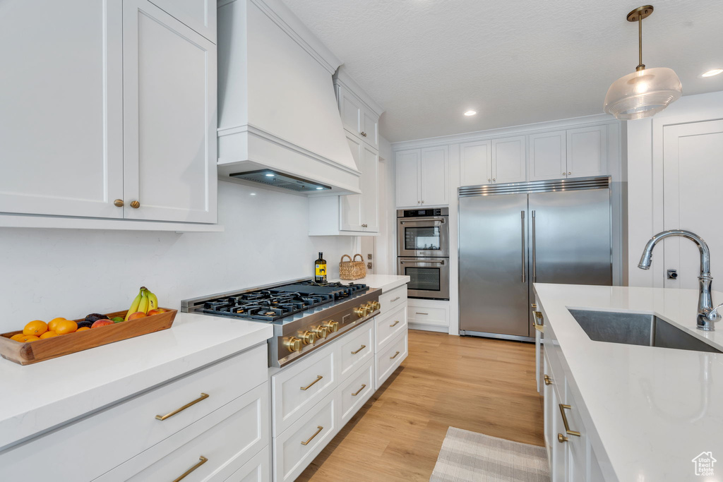Kitchen featuring appliances with stainless steel finishes, custom range hood, white cabinets, light countertops, and recessed lighting