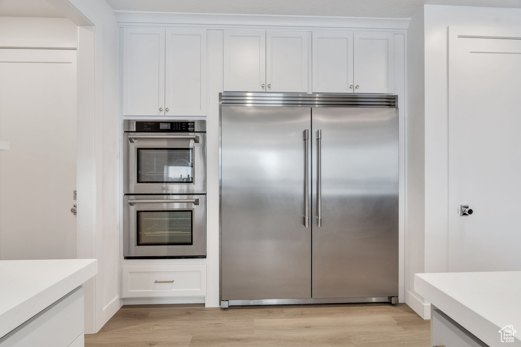 Kitchen with appliances with stainless steel finishes, light wood-type flooring, light countertops, and white cabinets