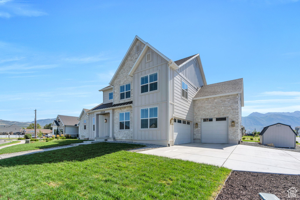 View of front of property with board and batten siding, concrete driveway, stone siding, a standing seam roof, and a front lawn