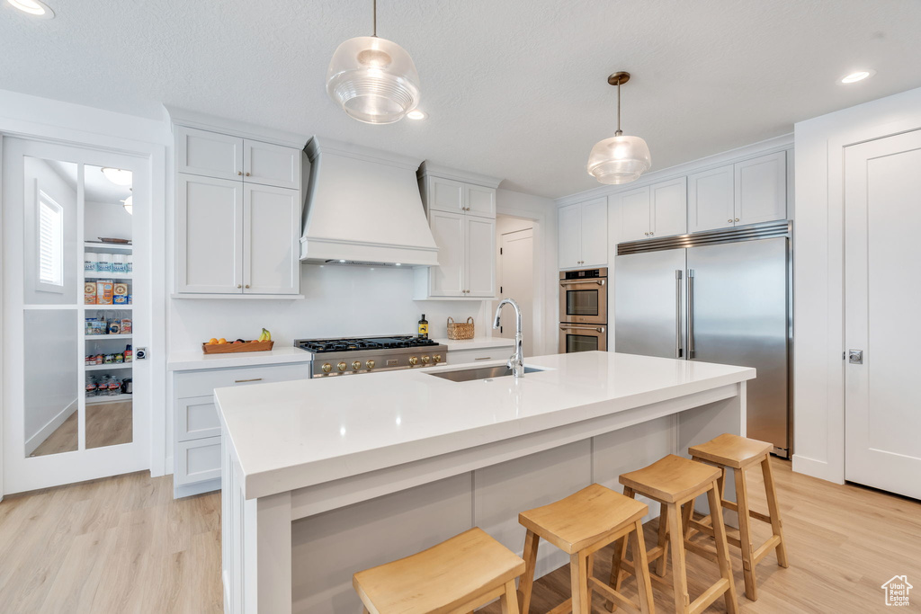 Kitchen with custom range hood, stainless steel appliances, light wood-style floors, light countertops, and recessed lighting