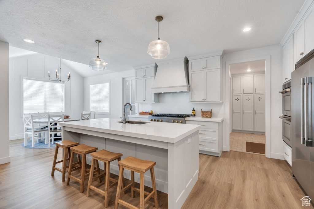Kitchen with premium range hood, light wood-style floors, light countertops, a breakfast bar area, and white cabinets