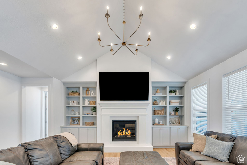 Living area featuring light wood-style floors, a chandelier, built in features, a glass covered fireplace, and vaulted ceiling