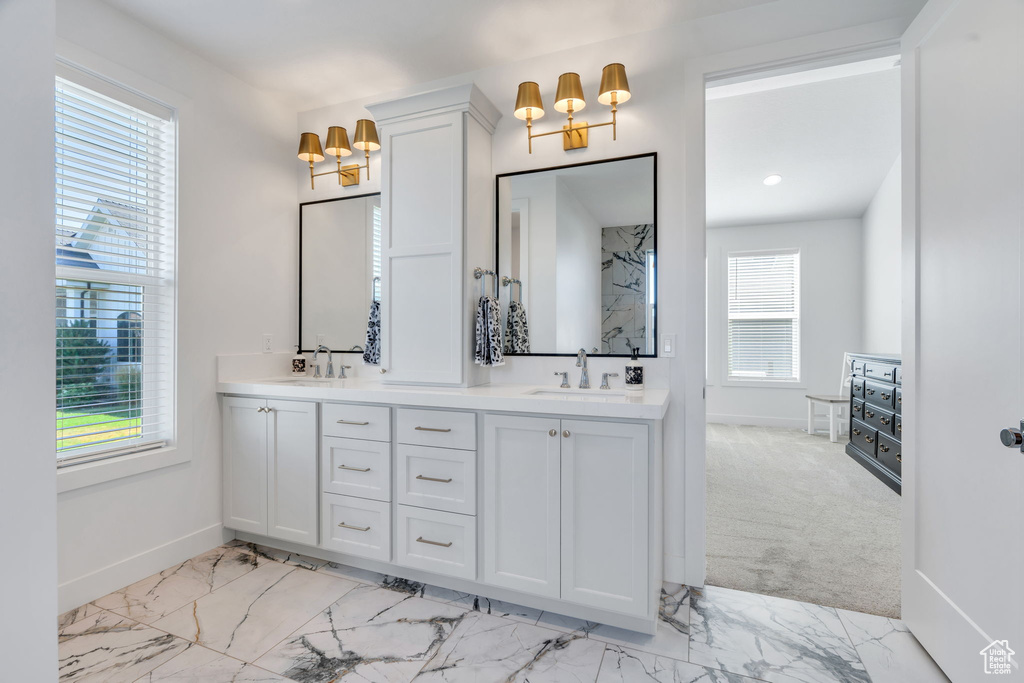 Full bath featuring a chandelier, healthy amount of natural light, double vanity, and marble look tiles