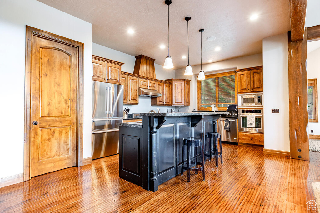 Kitchen featuring appliances with stainless steel finishes, under cabinet range hood, a kitchen breakfast bar, light wood-style flooring, and recessed lighting