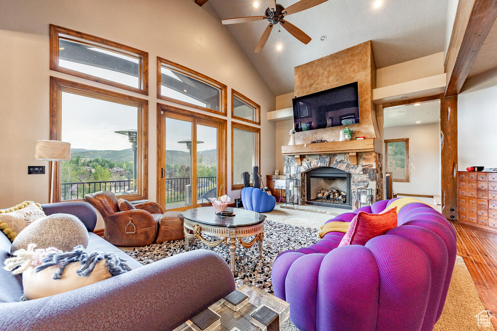 Living area with wood finished floors, healthy amount of natural light, a ceiling fan, high vaulted ceiling, and a stone fireplace
