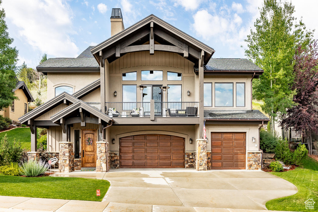 Craftsman-style home with a balcony, a garage, stone siding, a chimney, and driveway