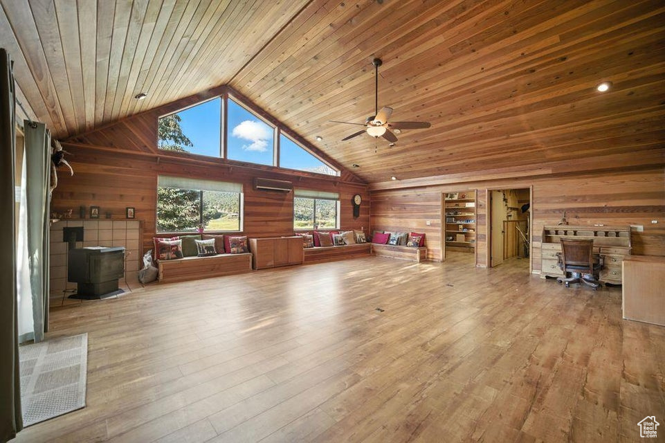 Living room with wooden walls, a wood stove, a ceiling fan, high vaulted ceiling, and hardwood / wood-style flooring