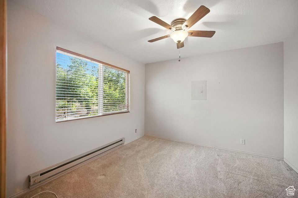 Spare room featuring a baseboard heating unit, carpet floors, a ceiling fan, and electric panel