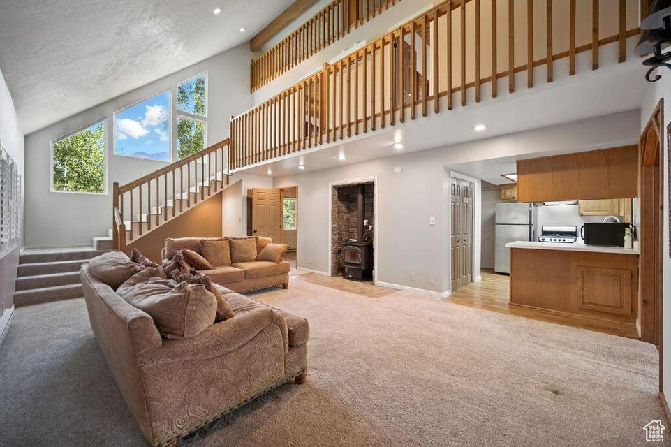 Living area featuring light colored carpet, stairway, high vaulted ceiling, a wood stove, and recessed lighting