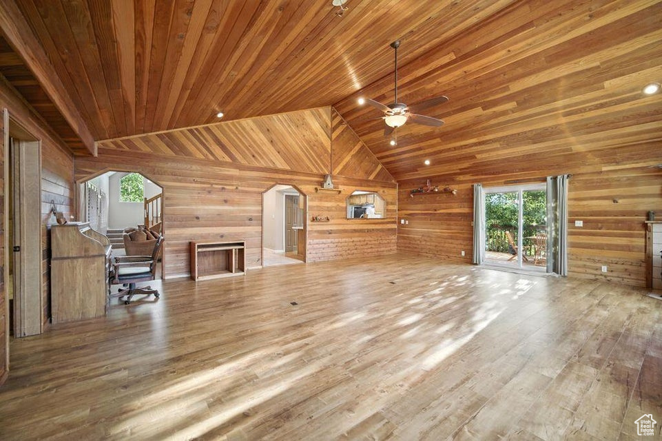 Unfurnished living room featuring wooden walls, ceiling fan, healthy amount of natural light, arched walkways, and wood finished floors