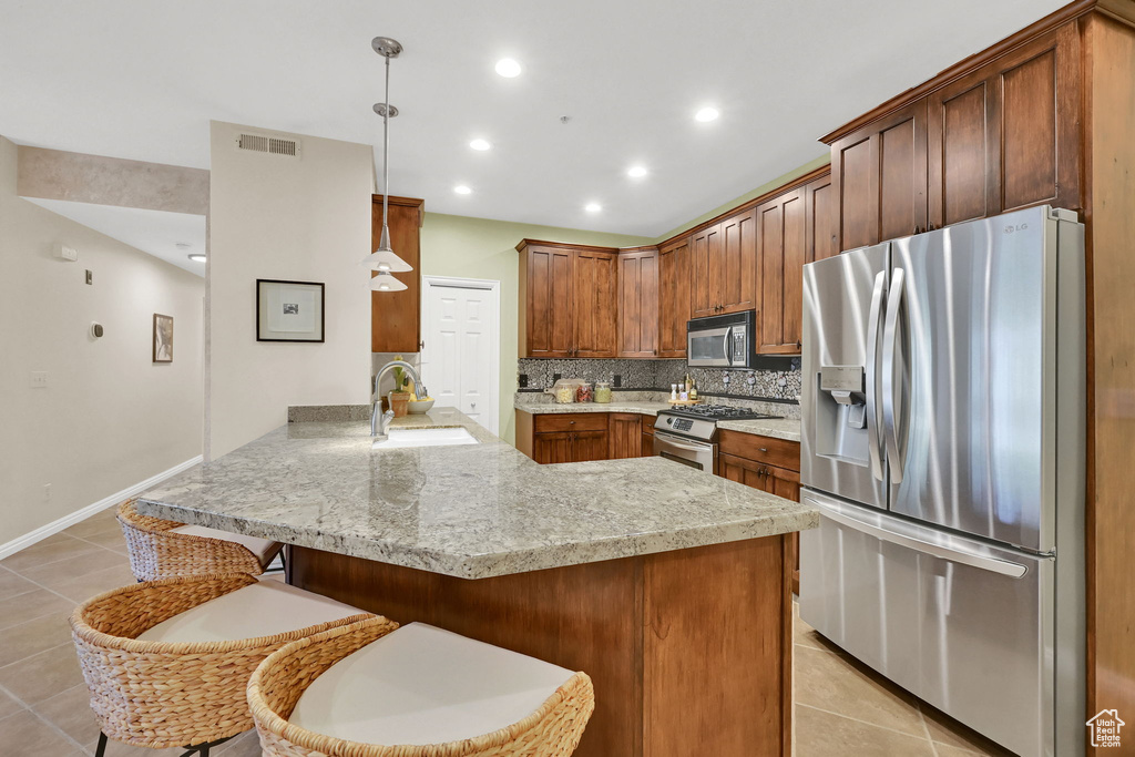 Kitchen featuring stainless steel appliances, a peninsula, light tile patterned flooring, a kitchen breakfast bar, and decorative backsplash