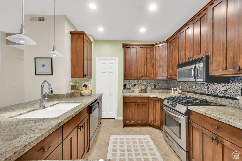 Kitchen with appliances with stainless steel finishes, light tile patterned flooring, backsplash, light stone countertops, and pendant lighting