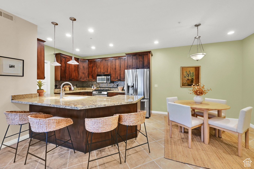 Kitchen with stainless steel appliances, a peninsula, tasteful backsplash, light stone countertops, and a kitchen breakfast bar