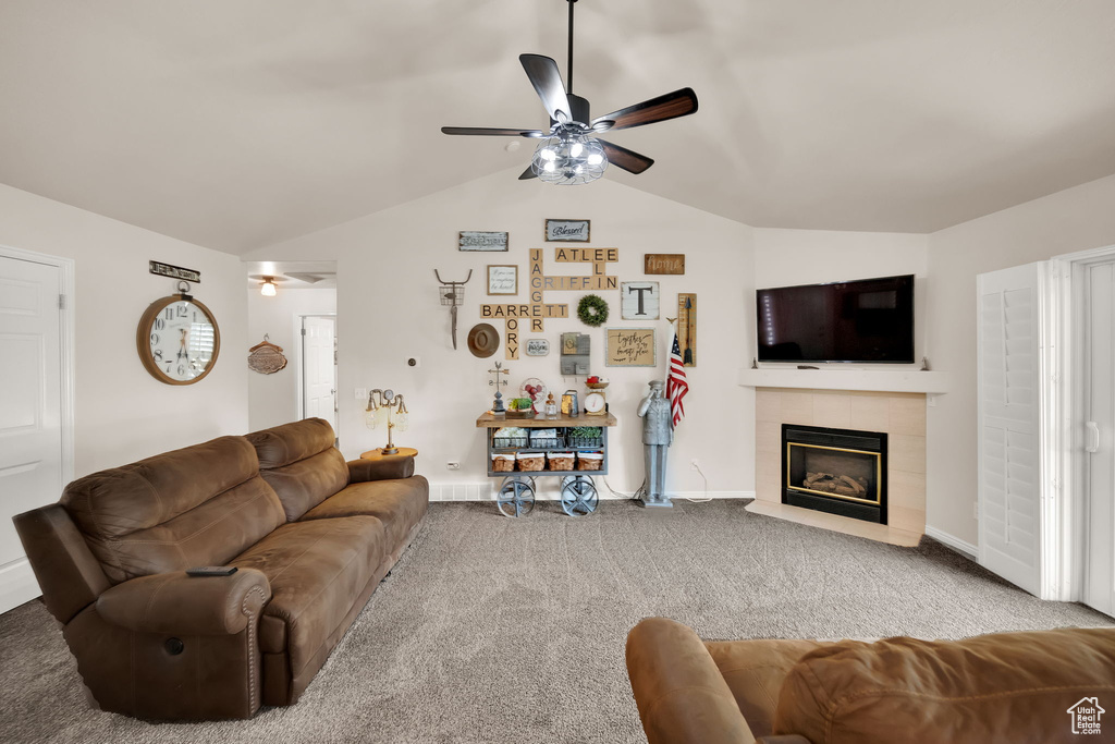 Carpeted living area featuring a ceiling fan, vaulted ceiling, and a tiled fireplace