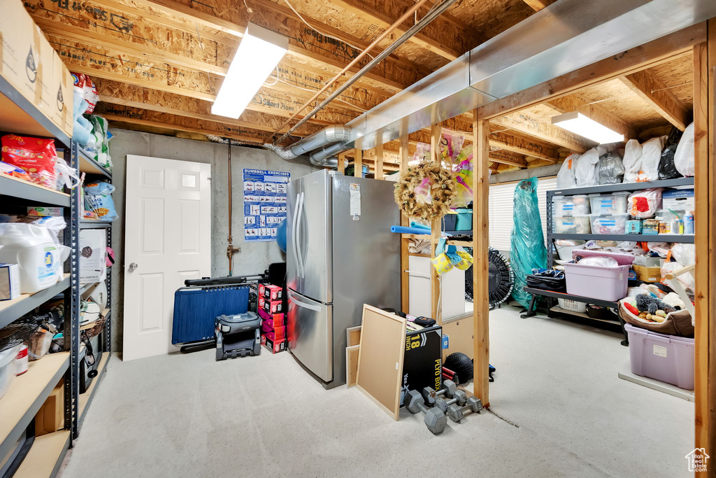 Unfinished below grade area featuring freestanding refrigerator and carpet flooring