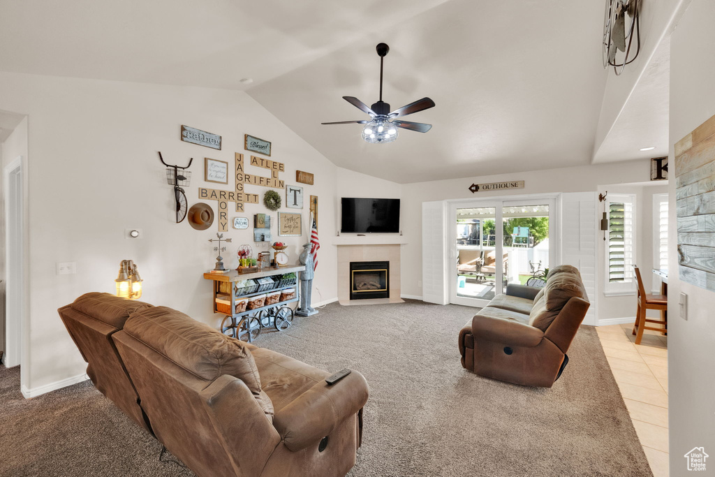 Living room with vaulted ceiling, a tile fireplace, ceiling fan, and light colored carpet