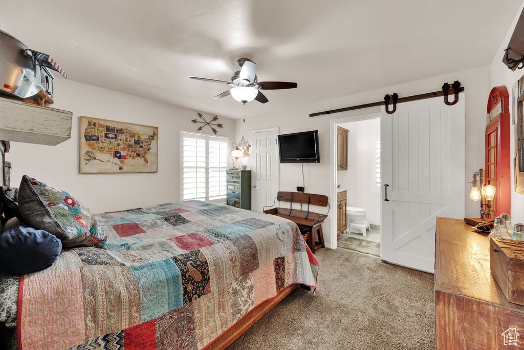 Bedroom featuring a barn door, carpet floors, ensuite bathroom, and a ceiling fan
