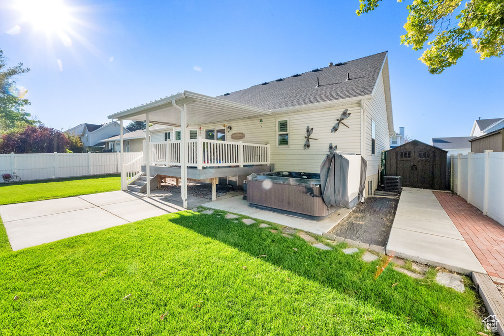 Rear view of house with a hot tub, a storage unit, a deck, a fenced backyard, and a patio area