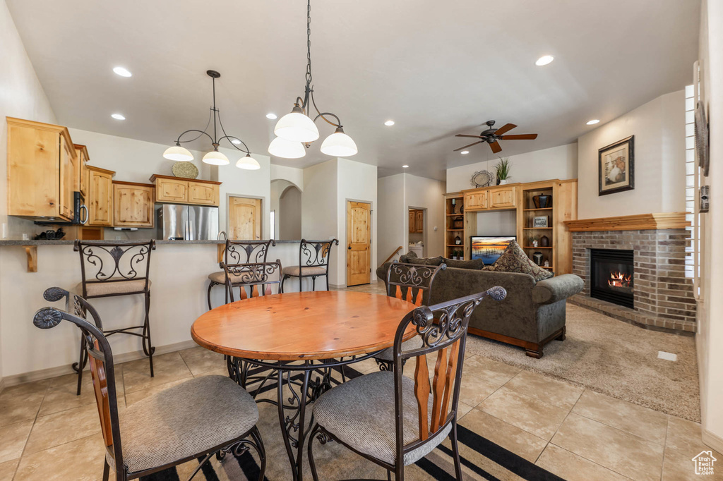 Dining space featuring a ceiling fan, recessed lighting, a brick fireplace, arched walkways, and light tile patterned floors
