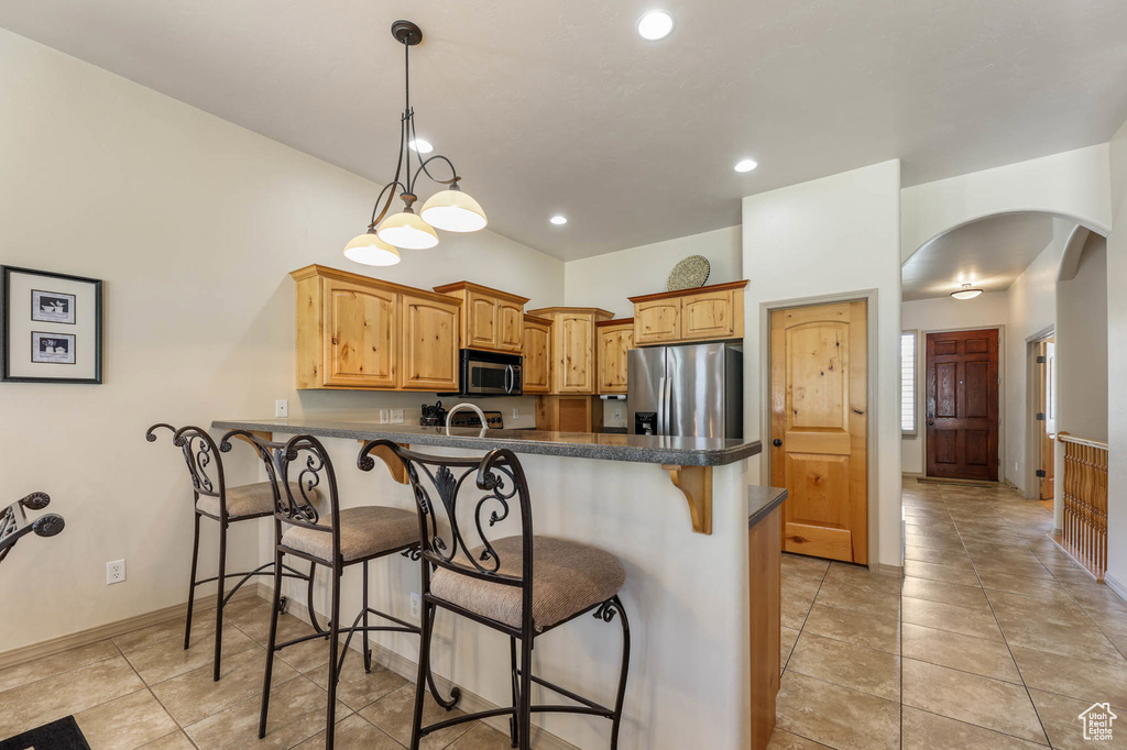 Kitchen with appliances with stainless steel finishes, arched walkways, a peninsula, dark countertops, and a breakfast bar area