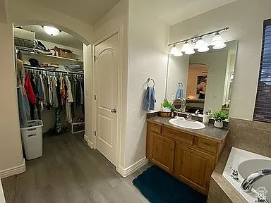 Bathroom with wood finished floors, a bath, vanity, and a spacious closet
