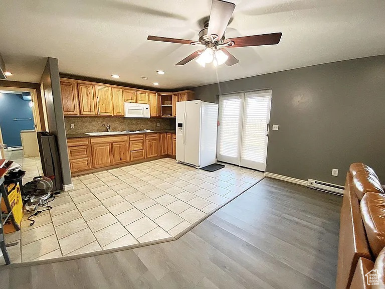 Kitchen featuring white appliances, a ceiling fan, dark countertops, a baseboard heating unit, and light wood-type flooring