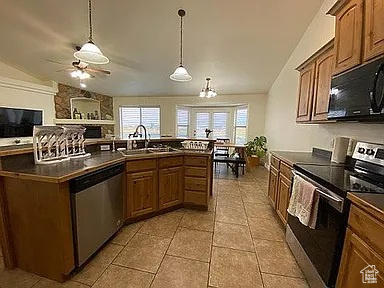 Kitchen featuring appliances with stainless steel finishes, vaulted ceiling, dark countertops, brown cabinets, and ceiling fan