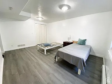 Bedroom featuring wood finished floors, baseboard heating, and a closet