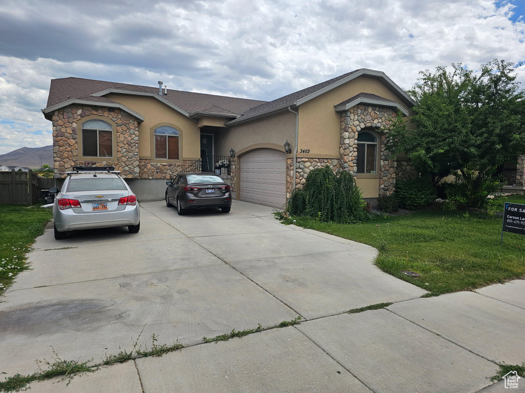 Ranch-style home with stone siding, stucco siding, concrete driveway, a garage, and a front yard