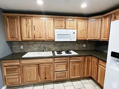 Kitchen with white appliances, decorative backsplash, dark countertops, light tile patterned floors, and recessed lighting