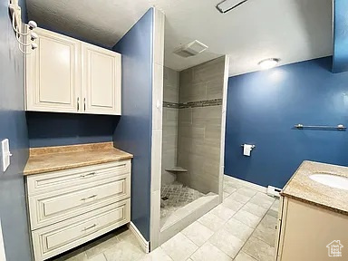 Full bath with vanity, tiled shower, and tile patterned floors
