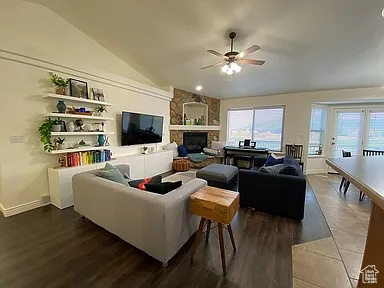 Living area with lofted ceiling, a ceiling fan, a stone fireplace, and dark wood-style flooring