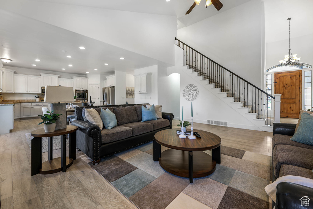 Living area featuring light wood-style flooring, a high ceiling, ceiling fan, stairs, and recessed lighting