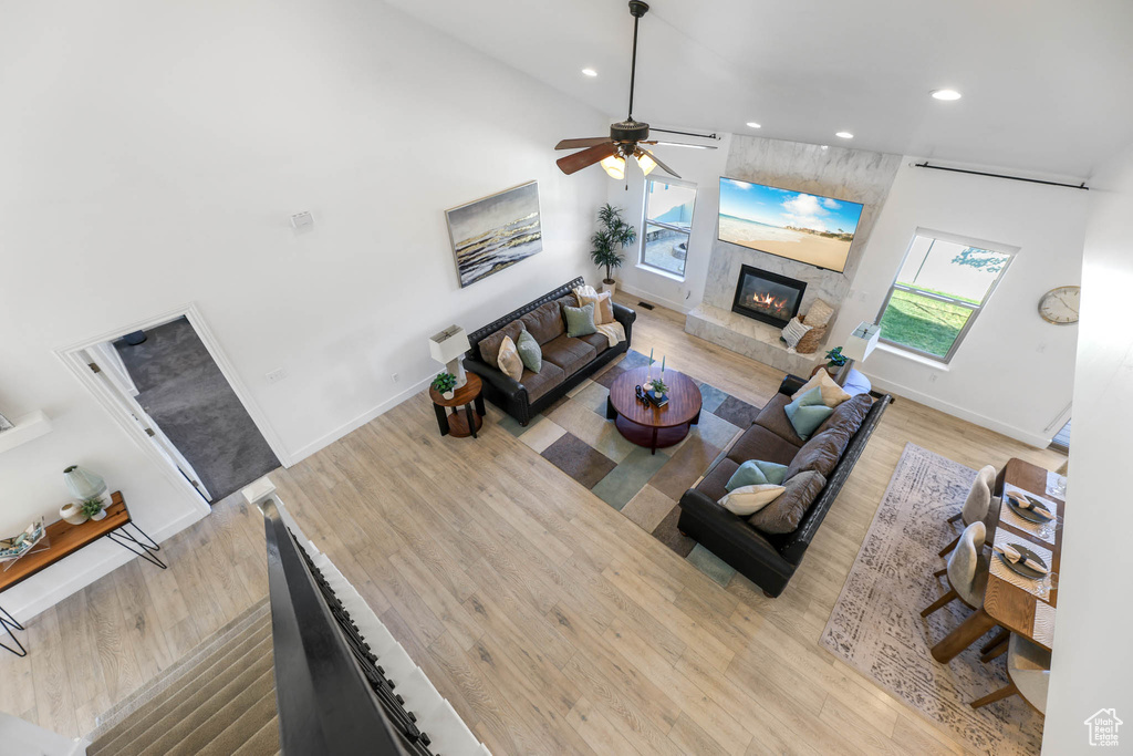 Living room featuring wood finished floors, recessed lighting, ceiling fan, a tiled fireplace, and a towering ceiling