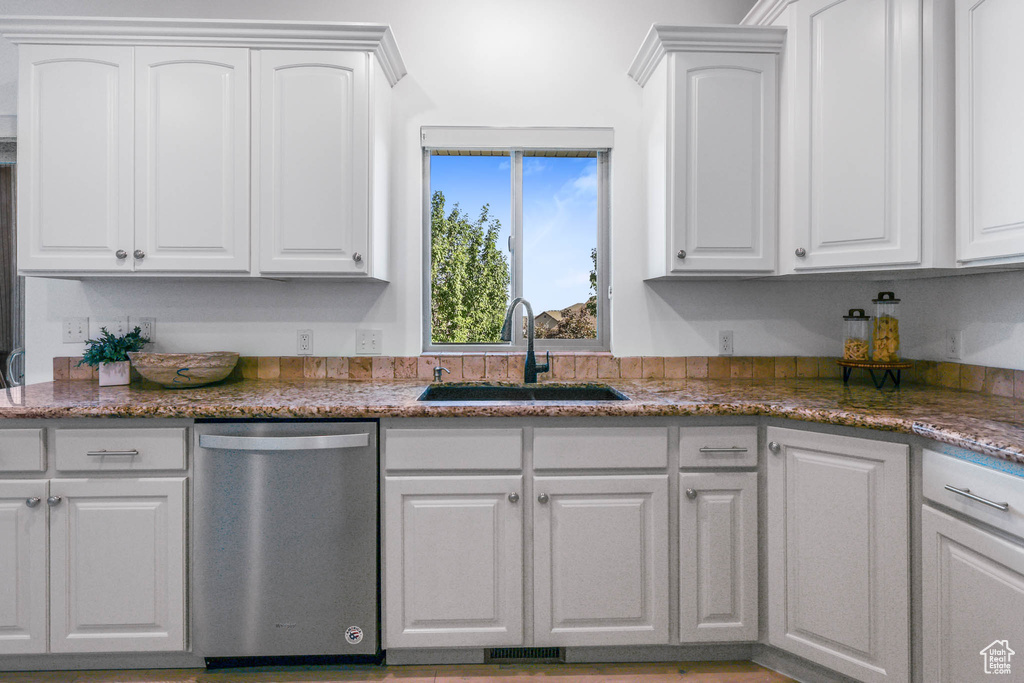 Kitchen featuring stainless steel dishwasher, white cabinetry, and stone countertops