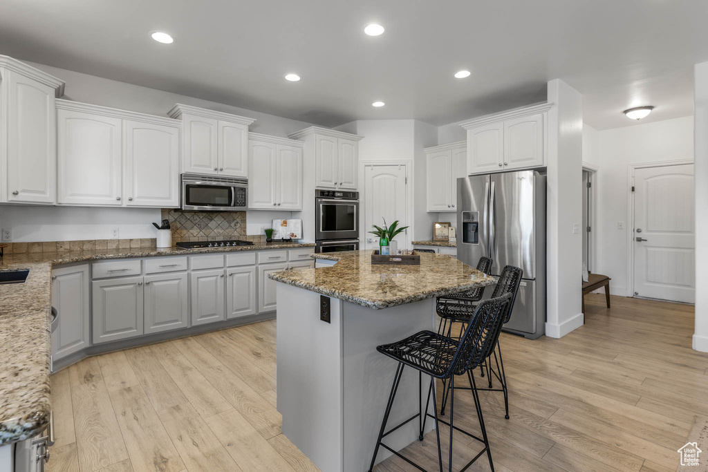 Kitchen with appliances with stainless steel finishes, a breakfast bar area, white cabinetry, stone countertops, and recessed lighting