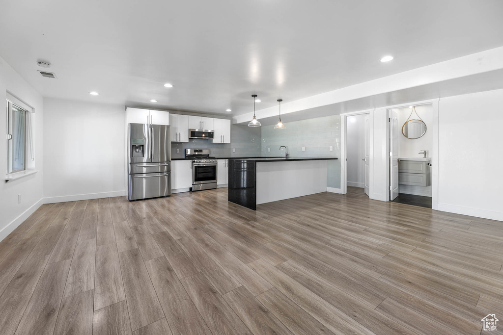 Kitchen with appliances with stainless steel finishes, dark countertops, white cabinets, open floor plan, and recessed lighting