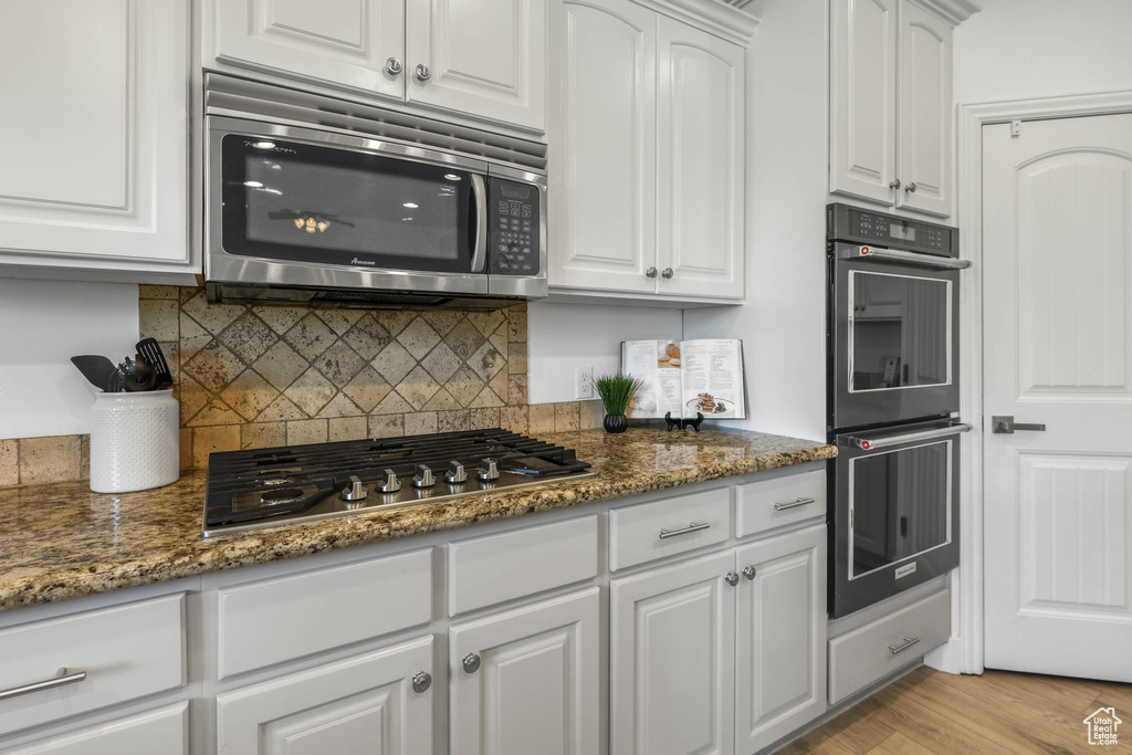 Kitchen featuring appliances with stainless steel finishes, white cabinets, decorative backsplash, and dark stone counters