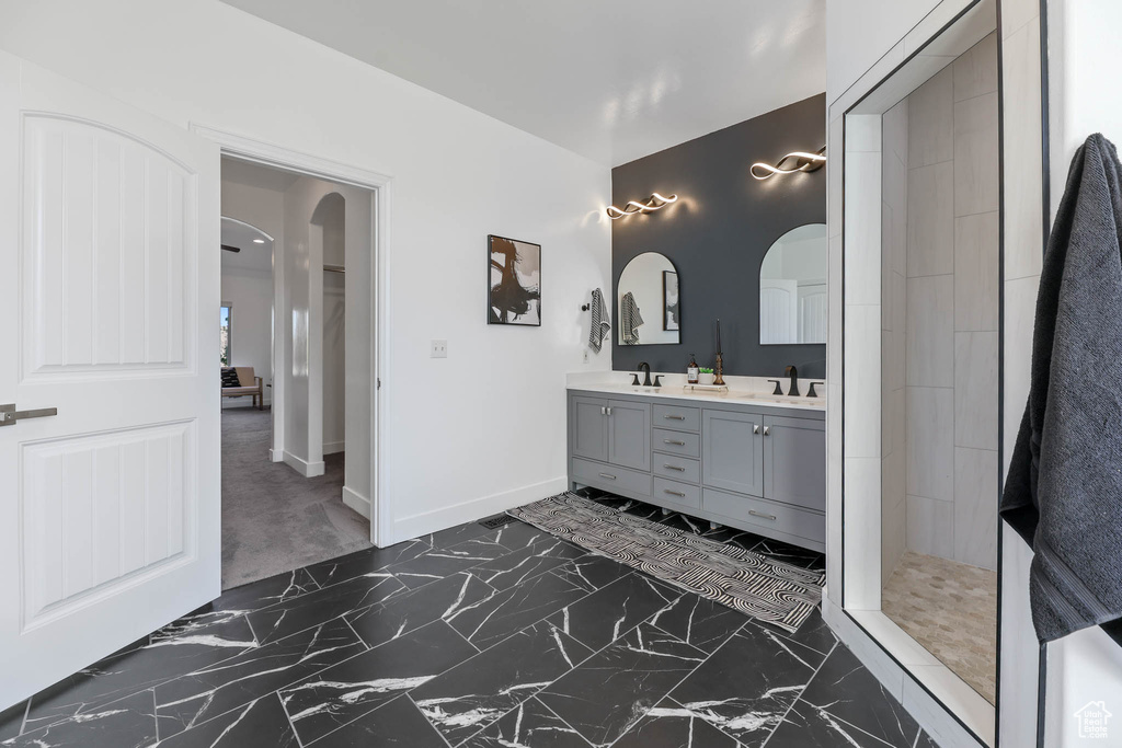 Bathroom with marble look tiles, double vanity, and tiled shower
