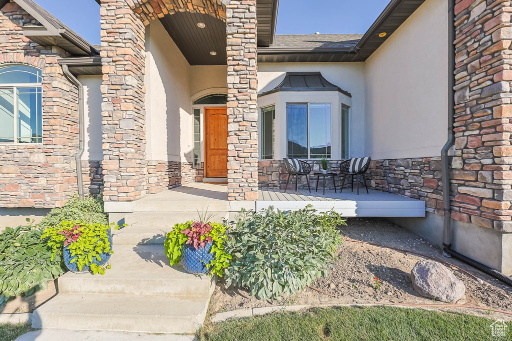 View of exterior entry featuring a porch, stucco siding, and stone siding