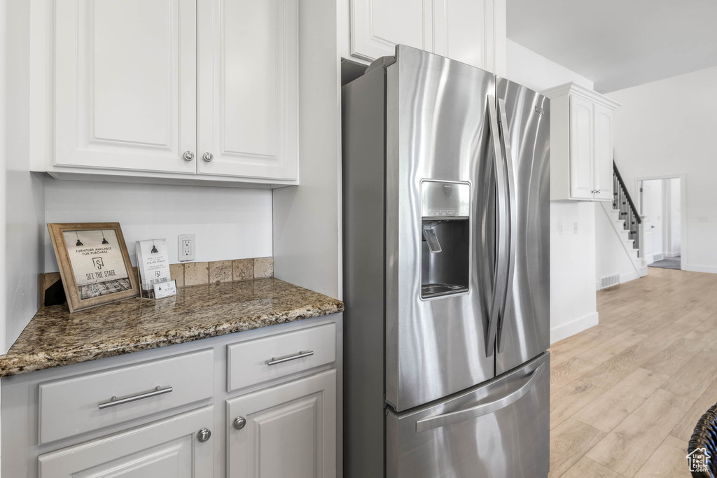 Kitchen featuring stainless steel refrigerator with ice dispenser, white cabinetry, light wood-style floors, and dark stone countertops