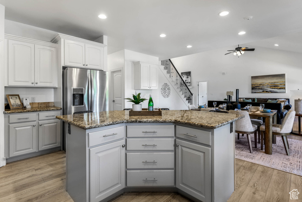 Kitchen featuring stainless steel refrigerator with ice dispenser, a center island, ceiling fan, gray cabinetry, and dark stone counters