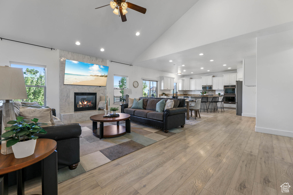 Living room featuring recessed lighting, light wood-style flooring, a fireplace, ceiling fan, and high vaulted ceiling