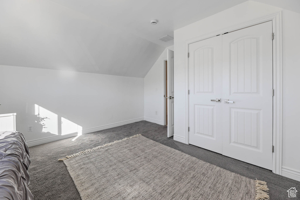 Unfurnished bedroom with dark colored carpet, lofted ceiling, and a closet