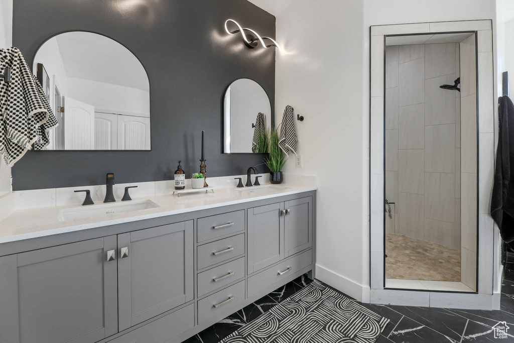 Full bathroom with tiled shower, double vanity, and marble finish flooring