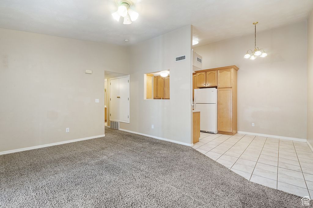 Unfurnished living room with a chandelier, vaulted ceiling, light carpet, and light tile patterned floors