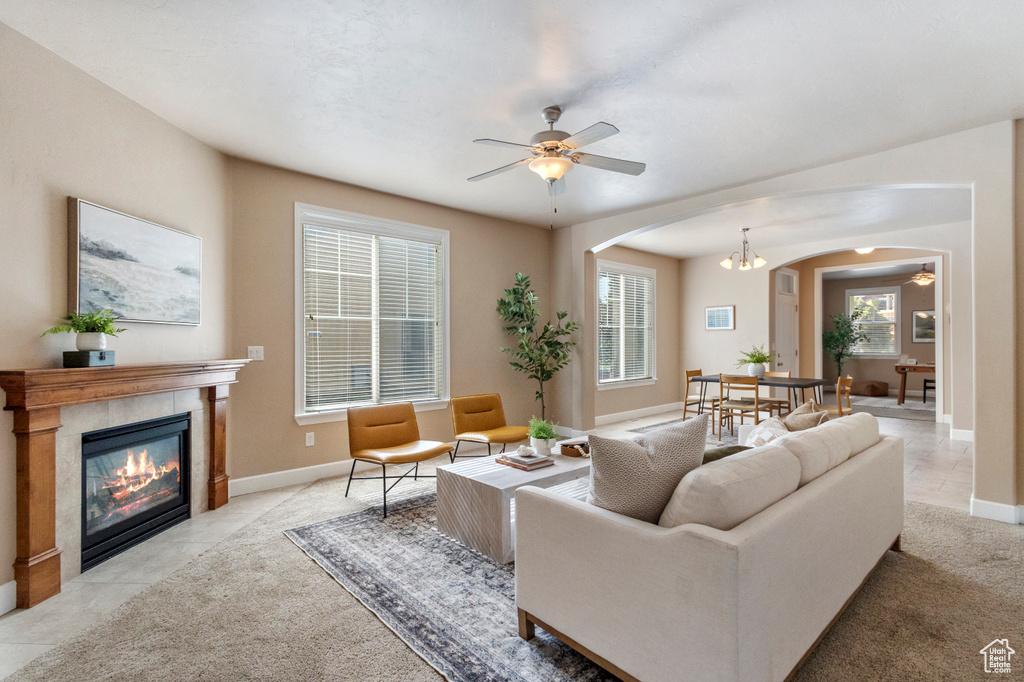 Living area with arched walkways, a ceiling fan, a tiled fireplace, and light carpet