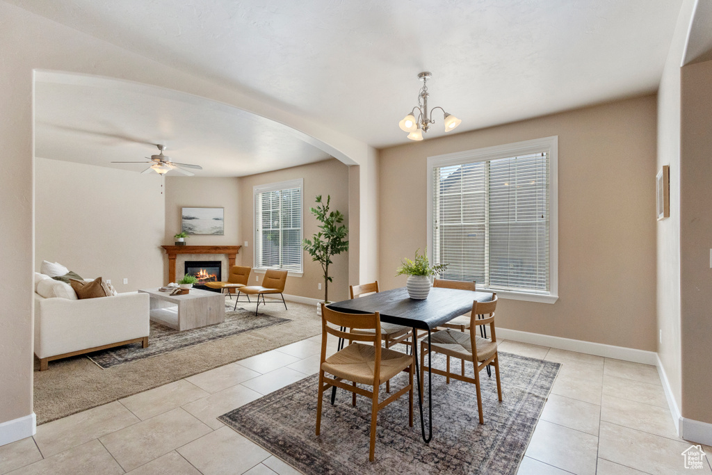 Dining room featuring a glass covered fireplace, light tile patterned floors, a ceiling fan, arched walkways, and a chandelier